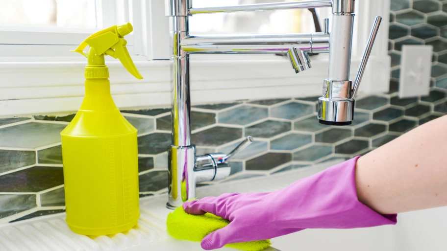 Hand scrubbing white sink with yellow sponge